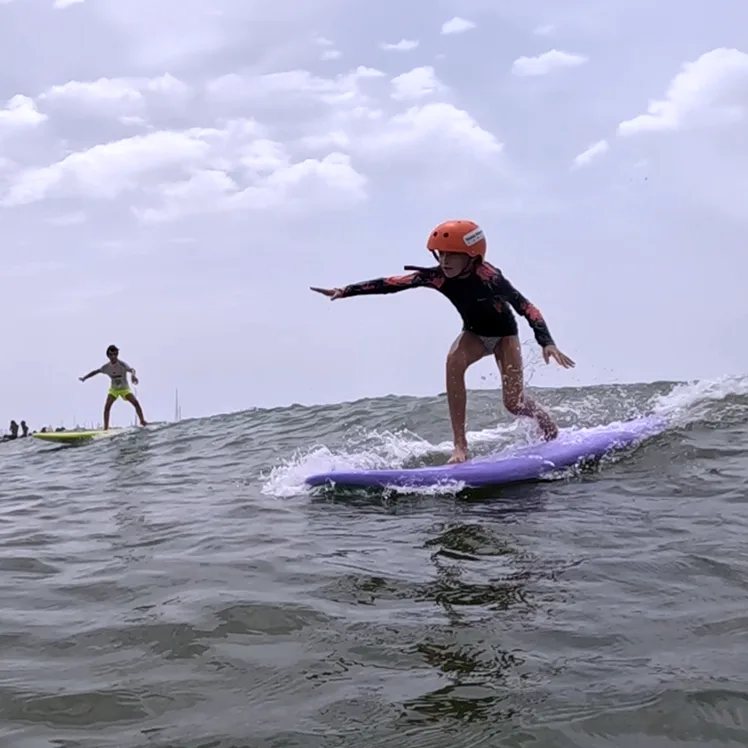 Niño surfeando una ola con casco en la clase de surf de Almerimar